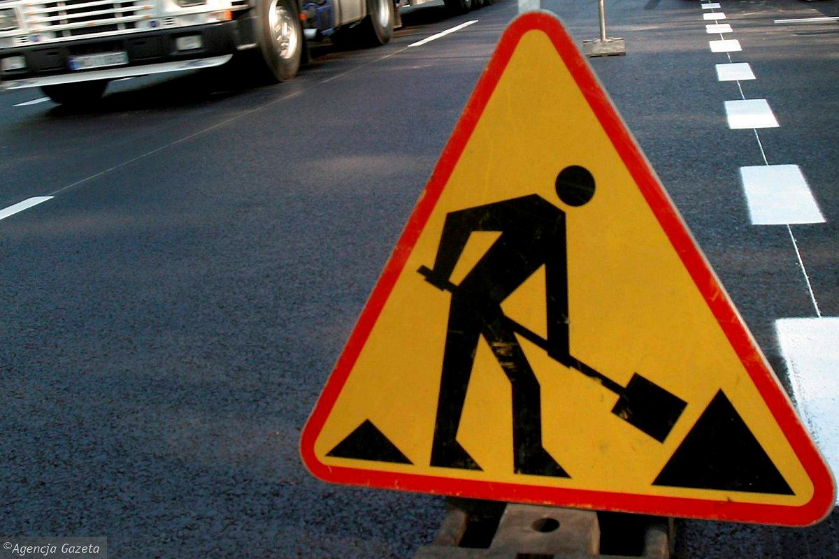 Grafika przedstawia znak drogowy informujący o trwających robotach drogowych. Znak znajduje się na jezdni.