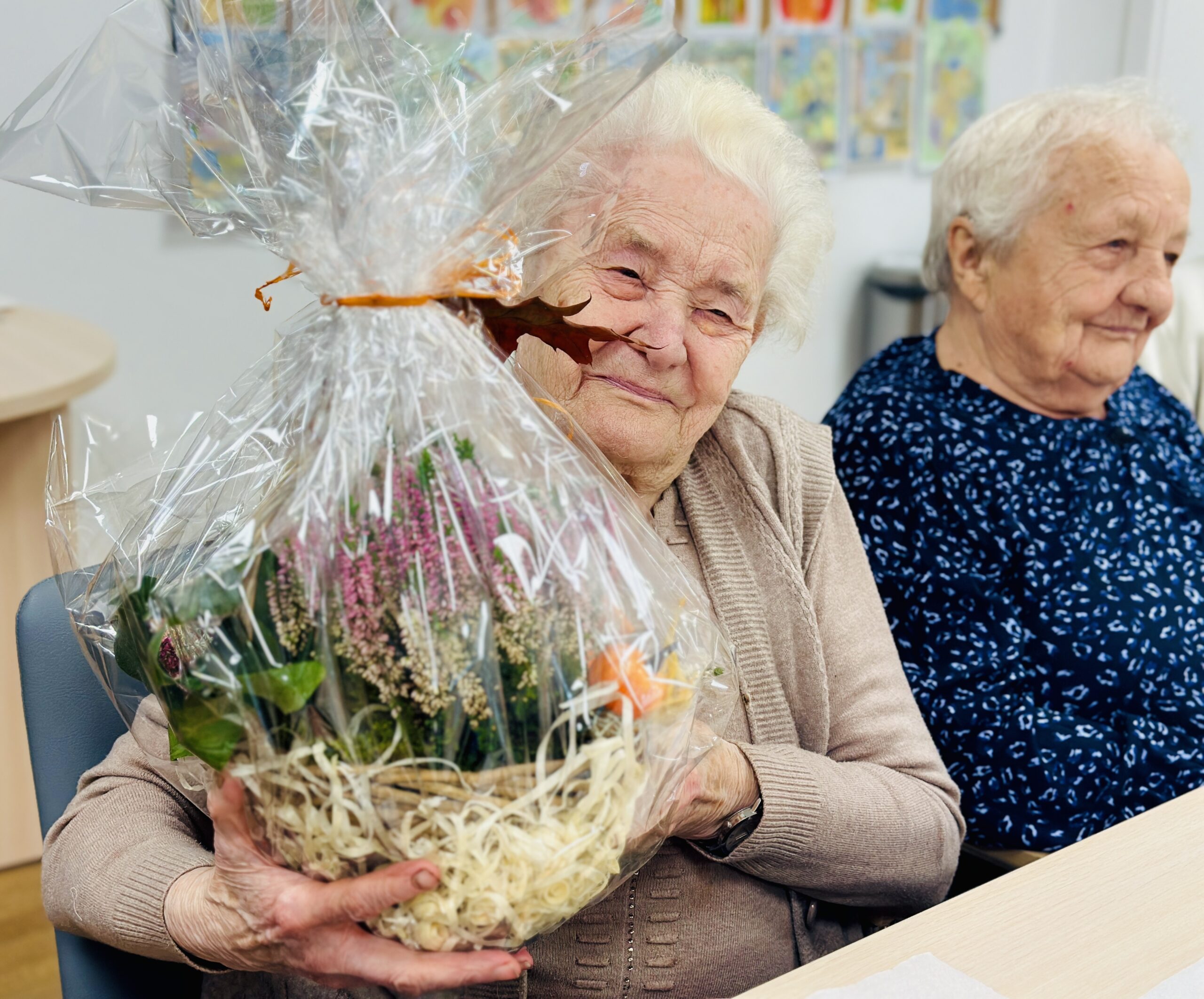 Zdjęcie przedstawia dwie uśmiechnięte seniorki. Jedna z nich trzyma w rękach upominek od wójta.