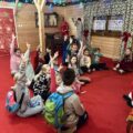 Zdjęcie przedstawia dzieci siedzące w półkole i zgłaszające się by odpowiedzieć św. Mikołajowi.