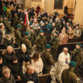 Zdjęcie ukazuje ludzi zebranych na uroczystości w kościele. Ksiądz proboszcz wchodzi do kościoła, a za nim podążają żołnierze.