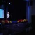 Na zdjęciu chłopiec na scenie recytujący swój wiersz. Za nim projektor, na którym widnieje napis: "XIII Gminny Konkurs Recytatorski Przedszkolaków". Scena ozdobiona kolorowymi dodatkami.
