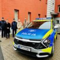 Zdjęcie przedstawia nowy radiowóz dla policji z odblaskowymi elementami. W tle Wójt Gminy Przemęt, policjanci z Powiatowej Policji w Wolsztynie oraz przedstawiciele samorządów lokalnych.