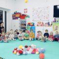 Włóczkowe cuda i lekcje dobroci. Żłobek w Błotnicy poznaje WOŚP. Zdjęcie przedstawia dzieci siedzące w półkole. Wykazują zainteresowanie kolorowymi włóczkami leżącymi na środku.