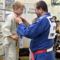 Zdjęcie przedstawia moment nałożenia jednemu z zwycięzców medalu na szyję. Chłopiec stoi na podium.
