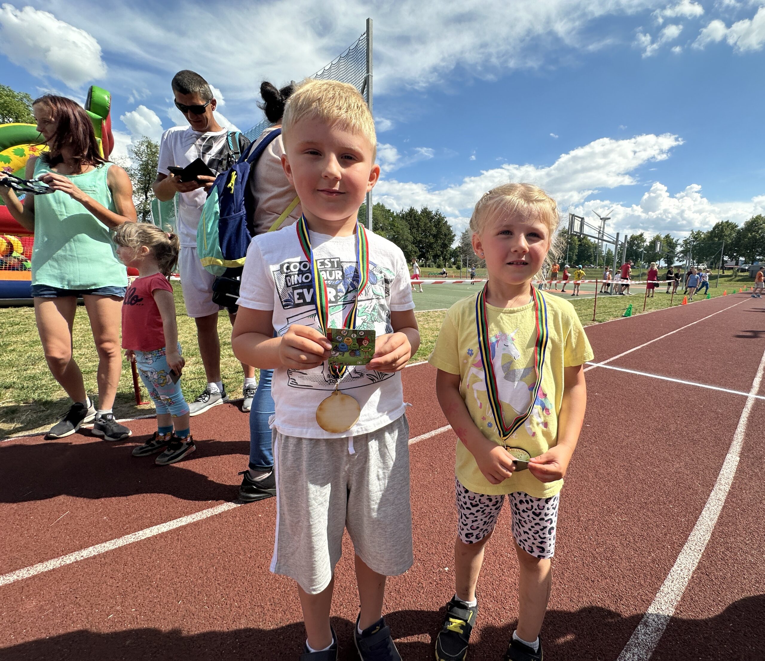 Zdjęcie przedstawia chłopca oraz dziewczynkę. Dzieci stoją na bieżni, na szyjach mają medale.