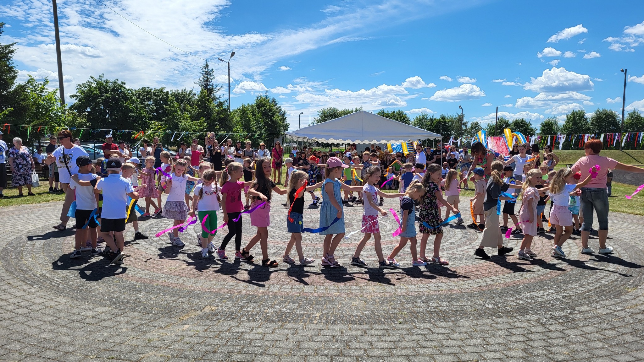 Na zdjęciu dzieci podczas jednej z zabaw tworząc kółko i trzymają w rękach kolorowe wstęgi.
