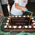 Zdjęcie przedstawia tort czekoladowy z dwoma racami. Na torcie widnieje napis " 25-lecie szkoły ponadpodstawowej w Przemęcie". Na zdjęciu uchwycono moment zapalania jednej z rac przez kobietę.