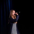 Na zdjęciu dziewczynka śpiewająca na scenie z sekcji SING.