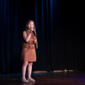 Na zdjęciu dziewczynka śpiewająca na scenie z sekcji SING.