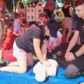 Zdjęcie przedstawia zajęcia z pierwszej pomocy przeprowadzane przez strażaka z PSP Wolsztyn. Dziewczynka na fotografii wykonuje uciskanie klatki piersiowej na fantomie.