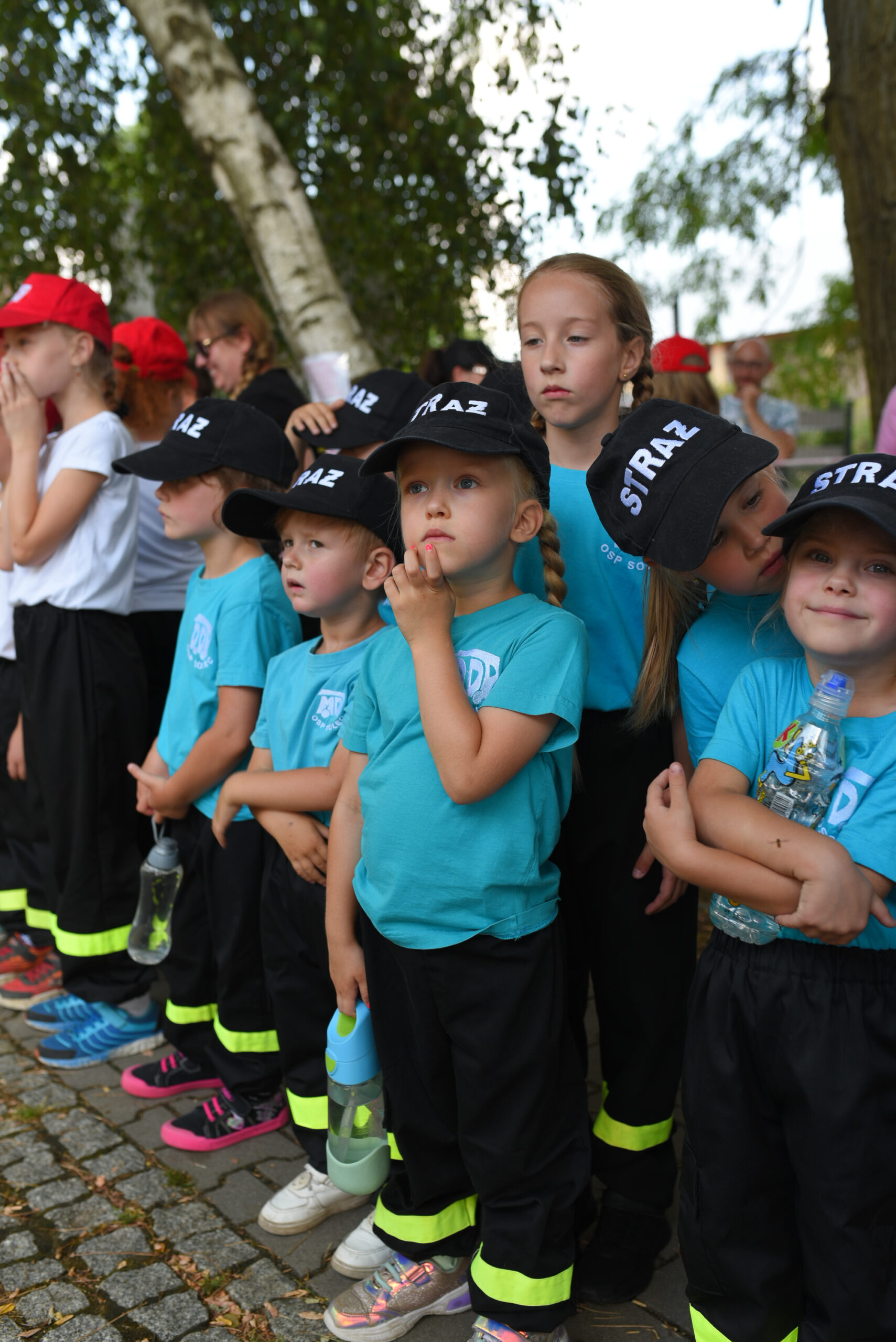 Zdjęcie przedstawia dzieci z OSP Solec ubrane w niebieskie bluzki i czarne czapki z daszkiem z białym napisem "straż".