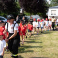 Na zdjęciu dzieci idą dwójkami wraz ze strażakiem z danej jednostki OSP.