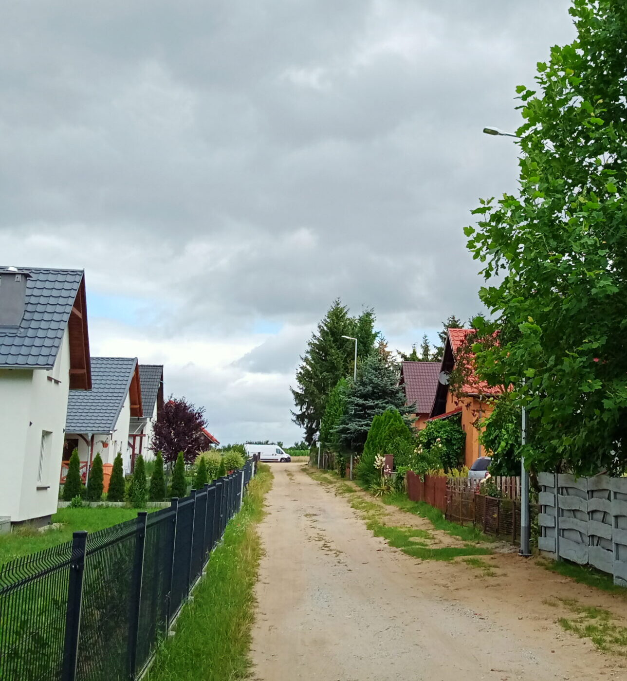 Zdjęcie przedstawia miejsce, w którym zostały postawione nowe lampy. Na fotografii uchwycono dwie nowe lampy ustawione w rzędzie. Oprócz tego na zdjęciu znajdują się też domy wraz z ogrodzeniami.