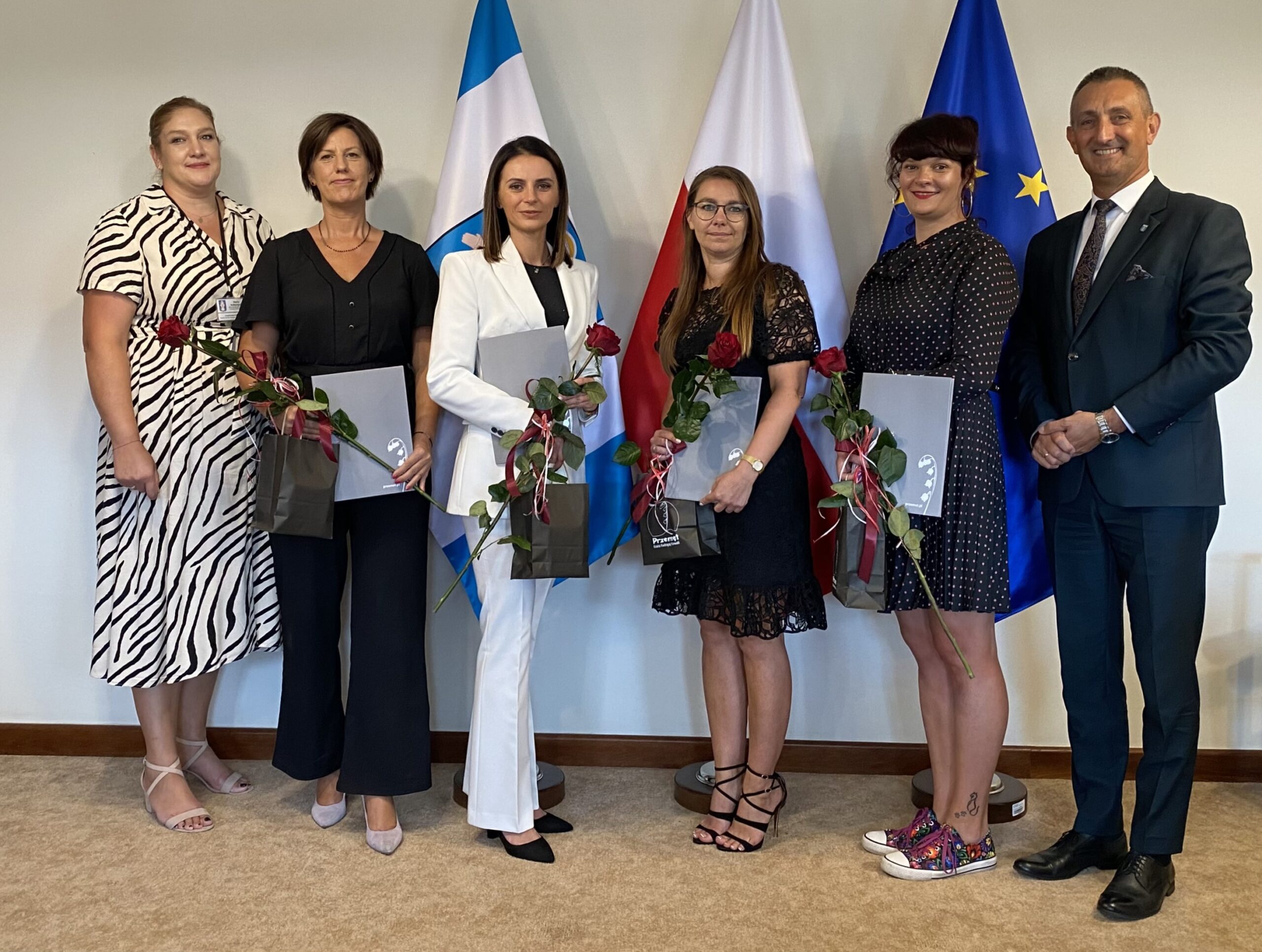 Na zdjęciu wójt, kierownik oświaty oraz nauczycielki. Wszyscy pozują w gabinecie na tle flag: polskiej, europejskiej oraz flagi z herbem gminy. Nauczycielki trzymają róże oraz awanse zawodowe na stopień nauczyciela mianowanego.