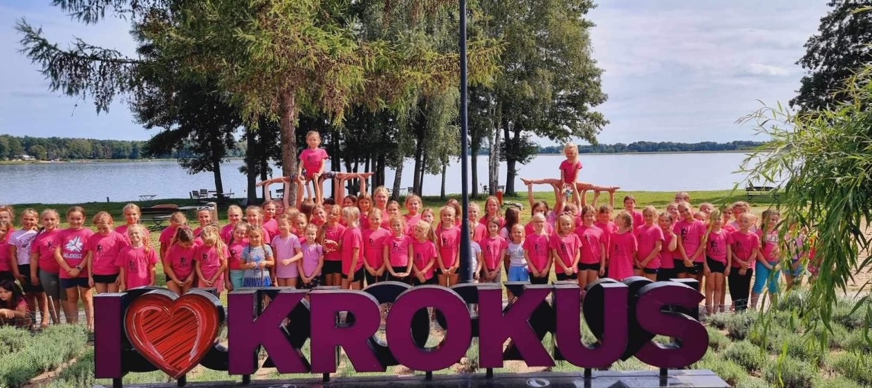 Grupowe zdjęcie mażoretek VENA przy dużym fioletowym napisie "I LOVE KROKUS".