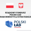 Grafika przedstawia szare tło, na górze znajduje się biało czerwona flaga oraz godło Polski, pod nimi widnieje napis: "Rządowy Fundusz Polski Ład Program Inwestycji Strategicznych". Pod nim została ukazana mapa Polski w niebieskich barwach. Koło mapy znajduje się napis "POLSKI ŁAD" , pod którym umieszczono biało-czerwoną linię.