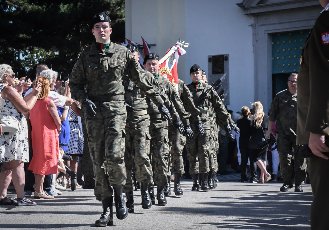 Na zdjęciu maszerujący żołnierze. Wokół ludzie.