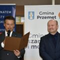 Na zdjęciu Zastępca Wójta Gminy Przemęt Waldemar Kalitka, który odczytuje list gratulacyjny. Obok niego stoi wicestarosta wolsztyński Mariusz Silski. W tle roll up gminy Przemęt oraz roll up: "Pod patronatem starosty wolsztyńskiego".