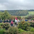 Grupa ludzi wraz z przewodnikiem. Wkoło drzewa i krzewy.