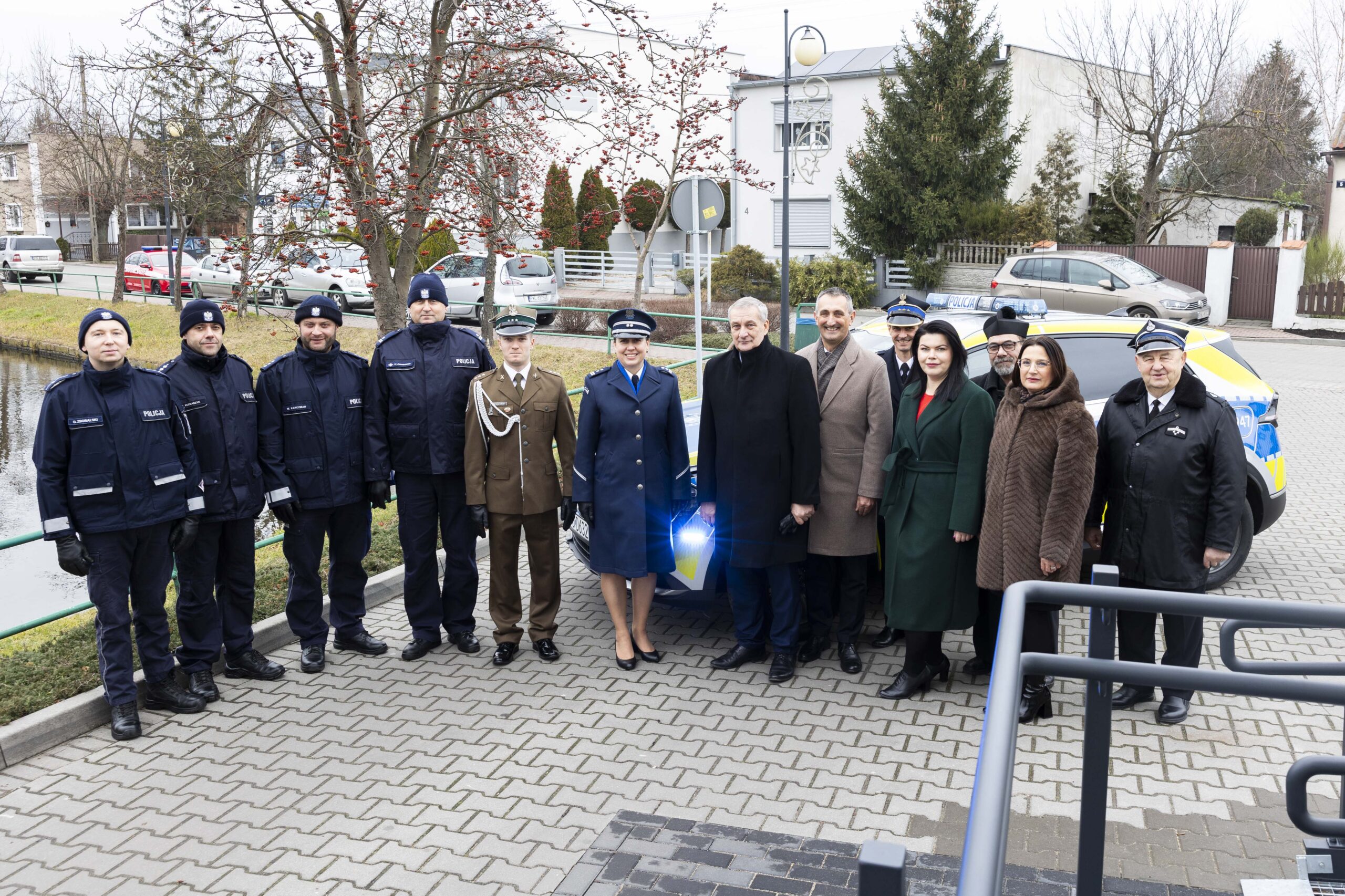 Na zdjęciu obecni na uroczystości: Minister Spraw Wewnętrznych i Administracji Wiesław Szczepański, Komendant Powiatowy Policji w Wolsztynie młodszy inspektor Katarzyna Sobaczk-Kukawka wraz z funkcjonariuszami, Komendant Powiatowy PSP w Wolsztynie kpt. Damian Glapiak, Przewodnicząca Rady Gminy Przemęt Monika Maćkowiak, Skarbnik Gminy Przemęt Bożena Ćwiklińska, por. 5 Lubuskiego Pułku Artylerii w Sulechowie Michał Brogowski, Prezes Zarządu Oddziału Gminnego Związku OSP RP w Przemęcie druh Józef Pauch oraz ks. Jarosław Kaczmarek. Wstęgę przecięli: Minister Spraw Wewnętrznych i Administracji Wiesław Szczepański, Wójt Gminy Przemęt Janusz Frąckowiak, Przewodnicząca Rady Gminy Monika Maćkowiak oraz Skarbnik Gminy Bożena Ćwiklińska. Poświęcenia sali dokonał ks. Jarosław Kaczmarek. Wszyscy pozują na tle nowego radiowozu.