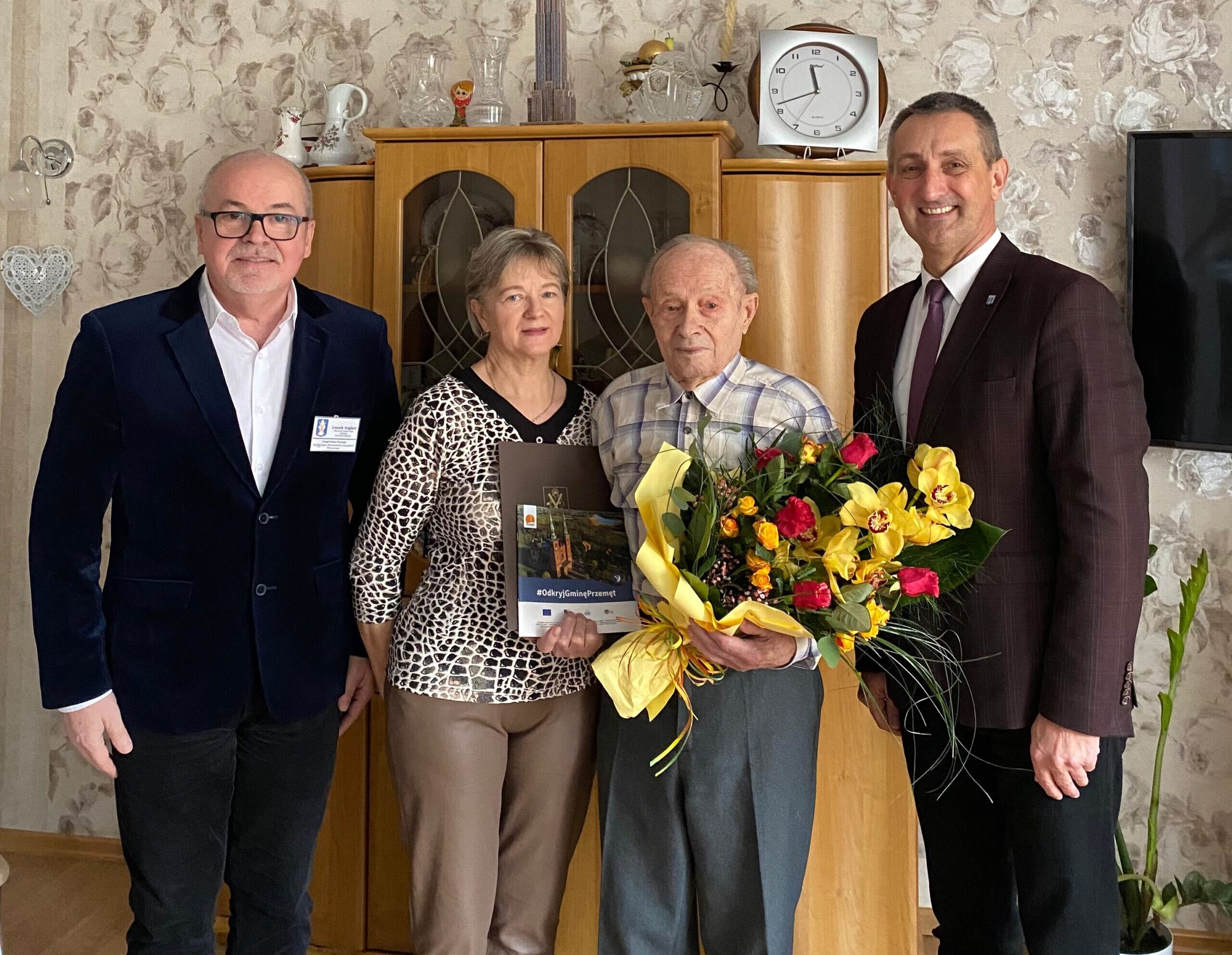 Wspólne zdjęcie, na którym znajdują się wójt gminy Janusz Frąckowiak, kierownik urzędu stanu cywilnego w Przemęcie Leszek Anglart, jubilat Pan Józef, który trzyma bukiet kwiatów, książkę o gminie Przemęt i list gratulacyjny, a także córka jubilata.