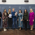 Wspólne zdjęcie, na którym znajdują się rodzice wraz z dzieckiem, wójt, przewodnicząca rady gminy, przedstawicielka Zarządu Powiatu Wolsztyńskiego Patrycja Pabich, Kierownik Urzędu Stanu Cywilnego Leszek Anglart, Zastępca Kierownika Urzędu Stanu Cywilnego Irena Mikołajczak oraz pracownik urzędu. Mama dziecka trzyma w rękach list oraz upominek. Wszyscy pozują na dużej szarej ściance, która zawiera herb gminy Przemęt oraz napisy "Gmina Przemęt".