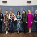 Wspólne zdjęcie, na którym znajduje się mama wraz z dzieckiem. Na fotografii także wójt, przewodnicząca rady gminy, przedstawicielka Zarządu Powiatu Wolsztyńskiego Patrycja Pabich, Kierownik Urzędu Stanu Cywilnego Leszek Anglart, Zastępca Kierownika Urzędu Stanu Cywilnego Irena Mikołajczak oraz pracownik urzędu. Wszyscy pozują na dużej szarej ściance, która zawiera herb gminy Przemęt oraz napisy "Gmina Przemęt".