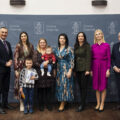 Wspólne zdjęcie, na którym znajduje się mama wraz z dwójką dzieci. Jedno z nich jest starsze. Na fotografii także wójt, przewodnicząca rady gminy, przedstawicielka Zarządu Powiatu Wolsztyńskiego Patrycja Pabich, Kierownik Urzędu Stanu Cywilnego Leszek Anglart, Zastępca Kierownika Urzędu Stanu Cywilnego Irena Mikołajczak oraz pracownik urzędu. Wszyscy pozują na dużej szarej ściance, która zawiera herb gminy Przemęt oraz napisy "Gmina Przemęt".