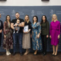 Wspólne zdjęcie, na którym znajdują się rodzice wraz z dzieckiem, wójt, przewodnicząca rady gminy, przedstawicielka Zarządu Powiatu Wolsztyńskiego Patrycja Pabich, Kierownik Urzędu Stanu Cywilnego Leszek Anglart, Zastępca Kierownika Urzędu Stanu Cywilnego Irena Mikołajczak oraz pracownik urzędu. Wszyscy pozują na dużej szarej ściance, która zawiera herb gminy Przemęt oraz napisy "Gmina Przemęt".