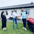 Zdjęcie ukazuje jak wójt gminy podaje dłoń prezesowi klubu sportowego. Na fotografii widoczna także radna Kinga Piędel oraz nowy traktor.