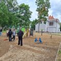 Zdjęcie przedstawia uczniów, którzy zagrabiają na placu zabaw.