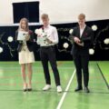 Na fotografii trójka uczniów przemawia podczas zakończenia roku. Dwójka z nich trzyma czerwone róże.