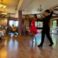 Na zdjęciu dwójka tancerzy podczas wykonywania jednej ze swoich choreografii tanecznych. Na zdjęciu widoczne także osoby, które obserwują widowisko.