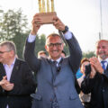 Na fotografii wójt Janusz Frąckowiak, który trzyma w górze statuetkę złotych szparagów. W tle inne osoby bijące brawo.