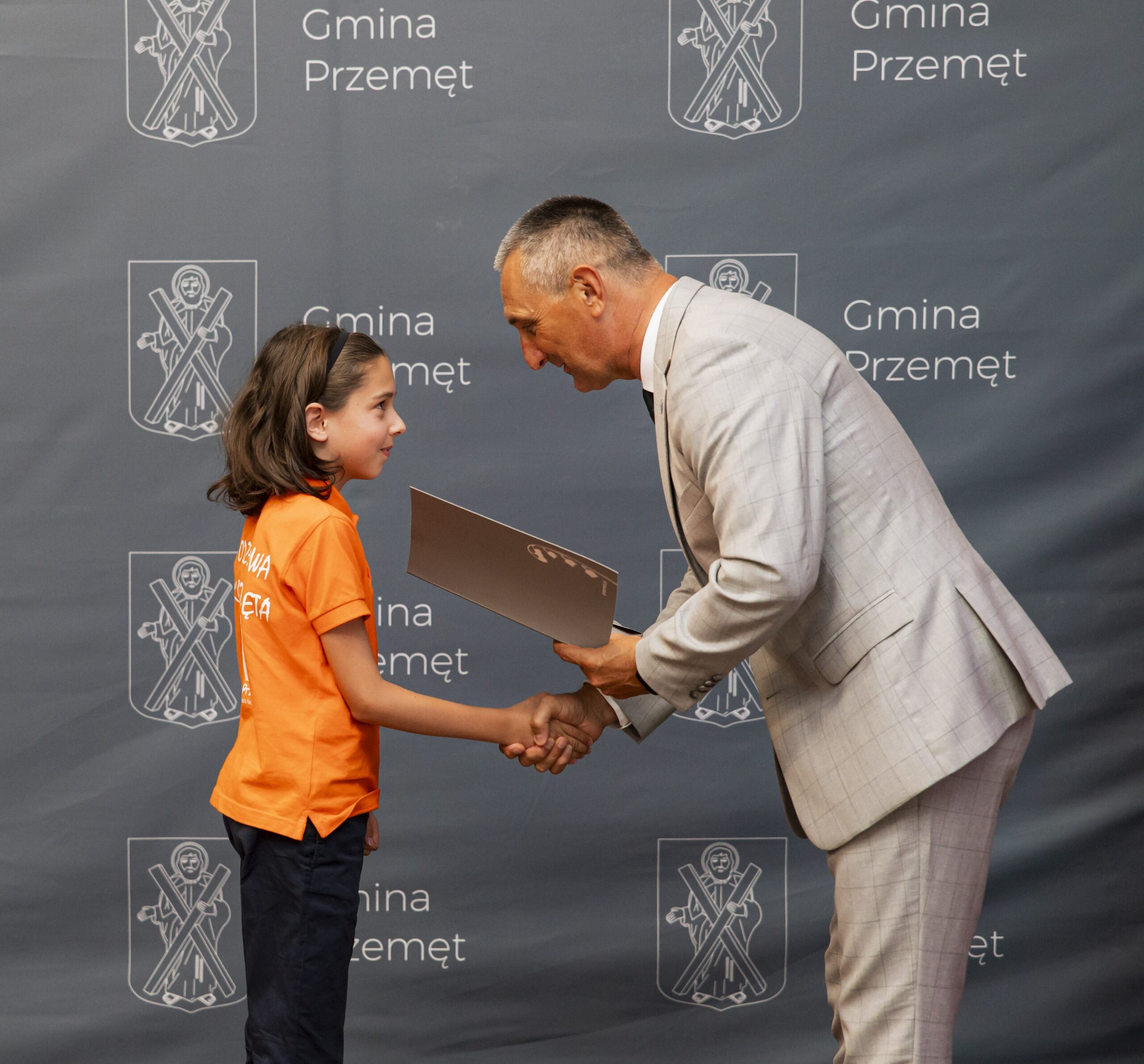 Na fotografii wójt wręcza nagrodę uczniowi. W tle ścianka gminy.