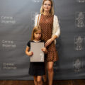 Na zdjęciu mama z córką, która pozuje do zdjęcia z nagrodą wójta. W tle ścianka.