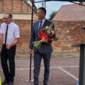 Na zdjęciu sołtys Perkowa Ilona Matysik wręcza kwiaty radnemu gminy Przemęt Szymonowi Wojciechowskiemu. Obok nich stoi wójt gminy również z bukietem w ręku. W tle – ceglana ściana i siatka ogrodzeniowa.