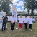 Na fotografii organizatorzy wydarzenia. Jeden z nich przemawia przez mikrofon. W tle windery informujące o honorowym patronacie wójta.