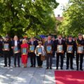 Do zdjęcia pozują wyróżnione osoby, w tym przedstawiciele lokalnych samorządów, instytucji oraz strażackich struktur ochotniczych. Osoby te trzymają w rękach pamiątkowe obrazy w ramach podziękowania za wsparcie i współpracę z Komendą Powiatową PSP w Wolsztynie.