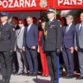 Na fotografii jeden ze strażaków, który przemawia podczas uroczystości. Koło niego stoi inny strażak. W tle przedstawiciele władz samorządowych i zaproszeni goście.