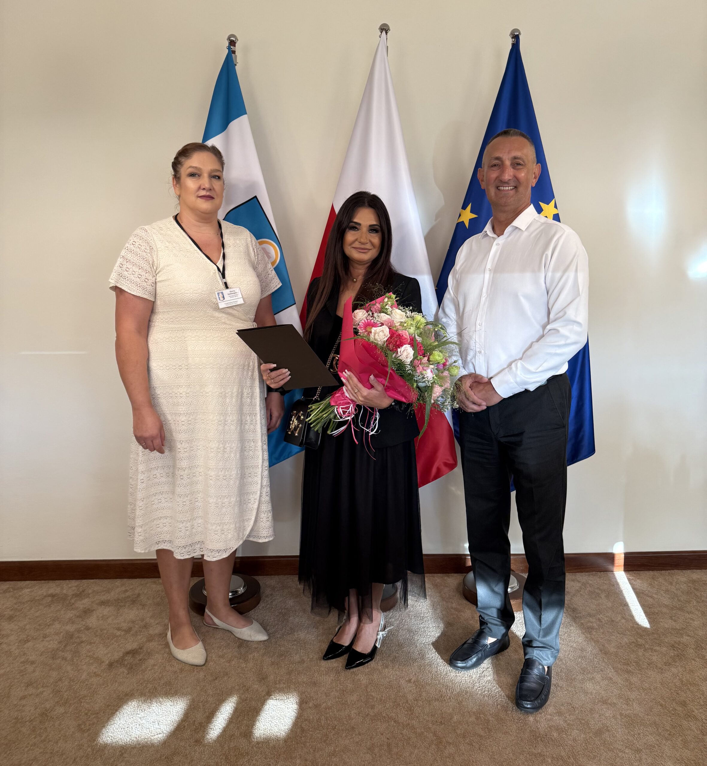 Na fotografii wójt, kierownik wydziału Oświaty i Sportu oraz Pani Edyta Kaczmarek - dyrektor przedszkola z Bucza, która trzyma w ręce list gratulacyjny oraz bukiet kwiatów.