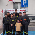 Do zdjęcia pozuje grupa strażaków z OSP oraz chłopiec z dziecięcej drużyny pożarniczej.