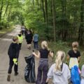 Na zdjęciu widać uczniów idących leśną drogą z workami na śmieci. Zbierają odpady z otoczenia.
