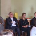 Na zdjęciu od lewej pani Marta Sobierajska, ksiądz, dyrektor szkoły Dagmara Nowak oraz wicedyrektor Piotr Kamiński. Wszyscy siedzą na sali.