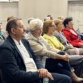Zebrani seniorzy siedzą na krzesłach i zainteresowaniem słuchają wykładu.