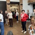 Grupa seniorów wraz z fizjoterapeutką wykonuje ćwiczenia.