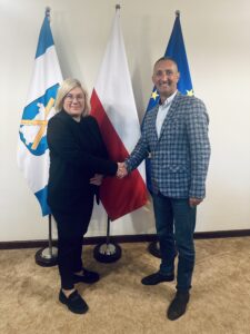 Na fotografii wójt podaje dłoń pani Annie Jackowskiej. Zdjęcie wykonano na tle flag: polskiej, europejskiej oraz flagi z herbem gminy Przemęt.