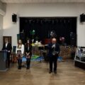 Na zdjęciu widoczny dyrektor szkoły podczas przemowy. Koło niego stoją uczniowie, którzy prowadzą uroczystość.