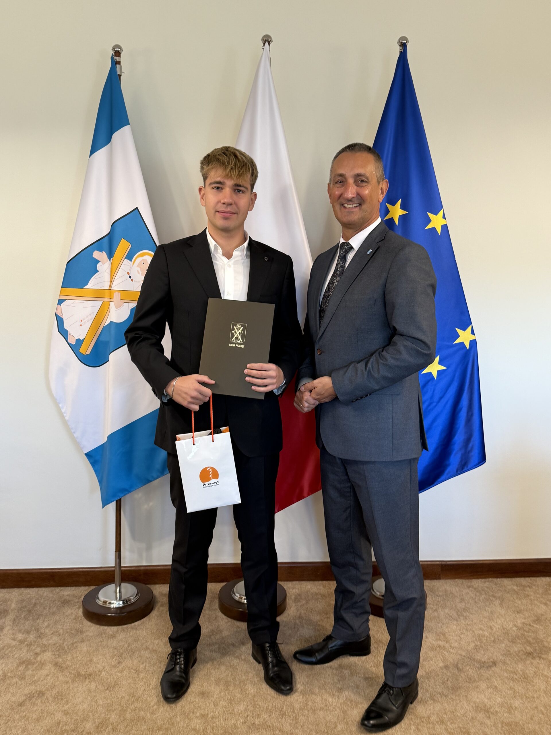 Na fotografii wójt i Alan Sadowski. Alan pozuje z czekiem i upominkiem.