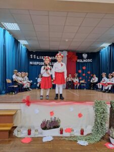 Na zdjęciu dwie dziewczynki podczas występu artystycznego. W tle inne dzieci.